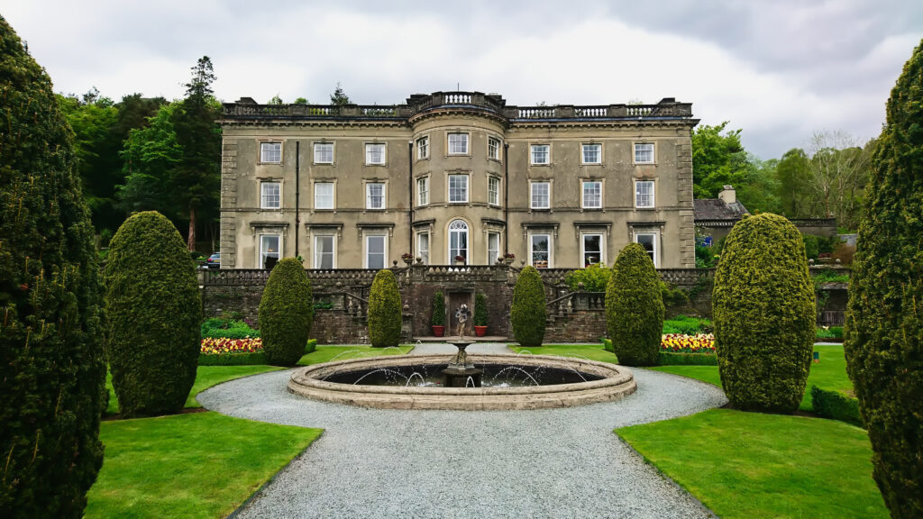 Rydal Hall and Gardens with a fountain in the front under a cloudy sky.